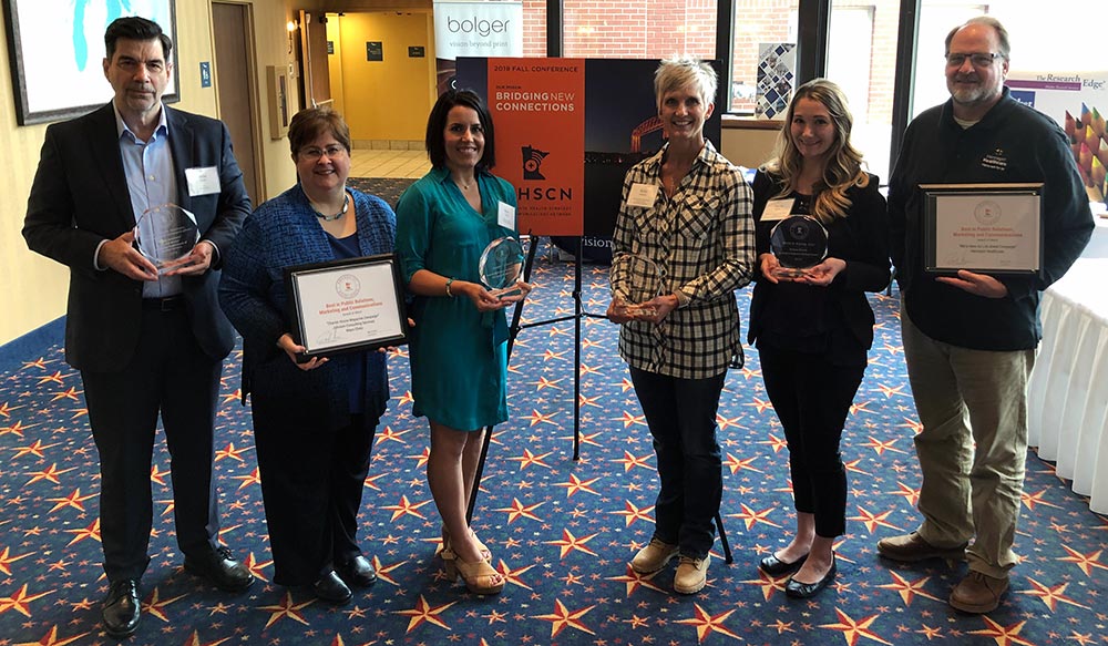 Six of the seven award winners pose with their awards in front of a sign with the 2019 Fall Conference theme